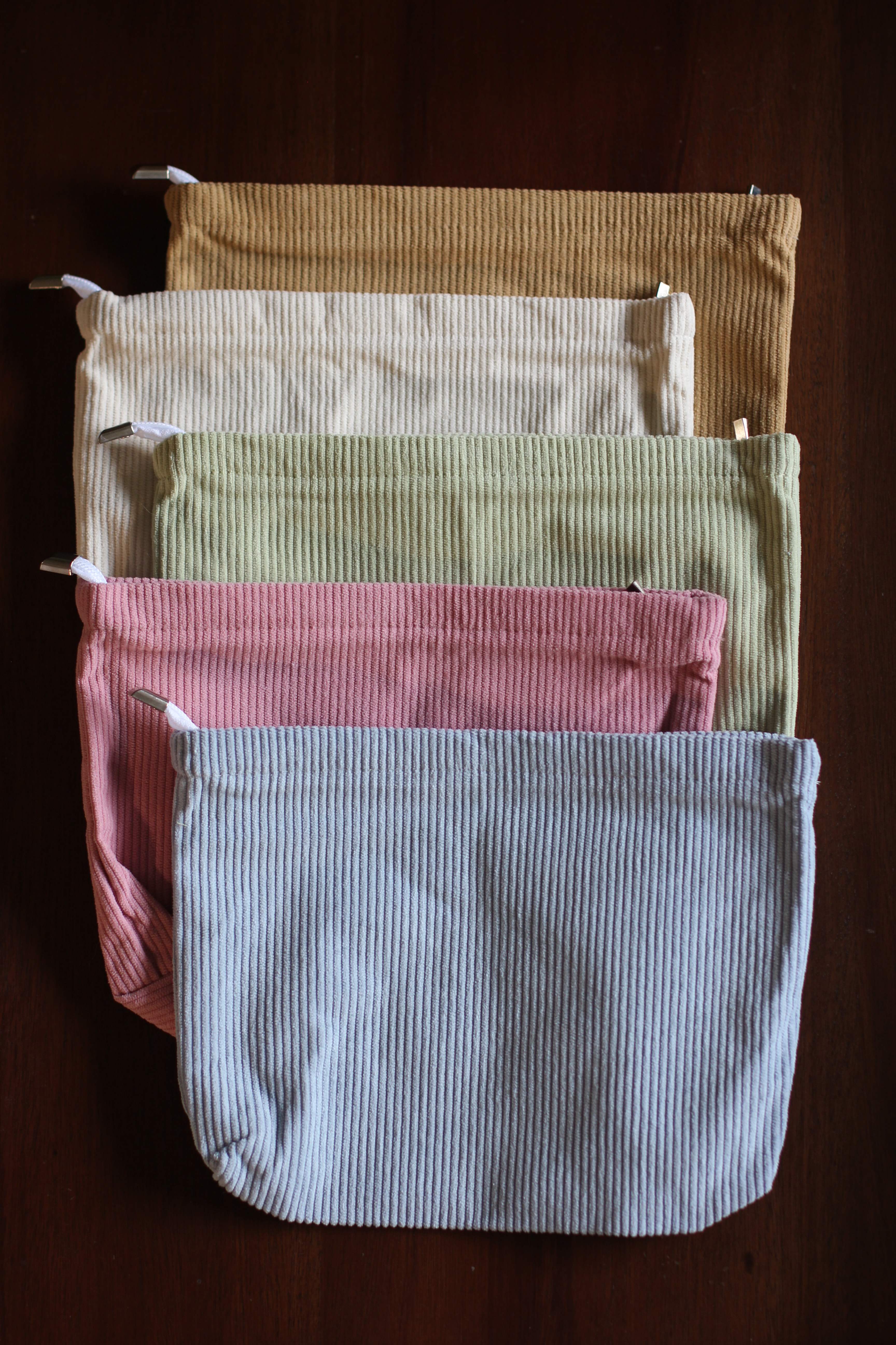 Five corduroy pouches from the Complete Labor Comfort Kit in tan, cream, sage, pink, and light blue