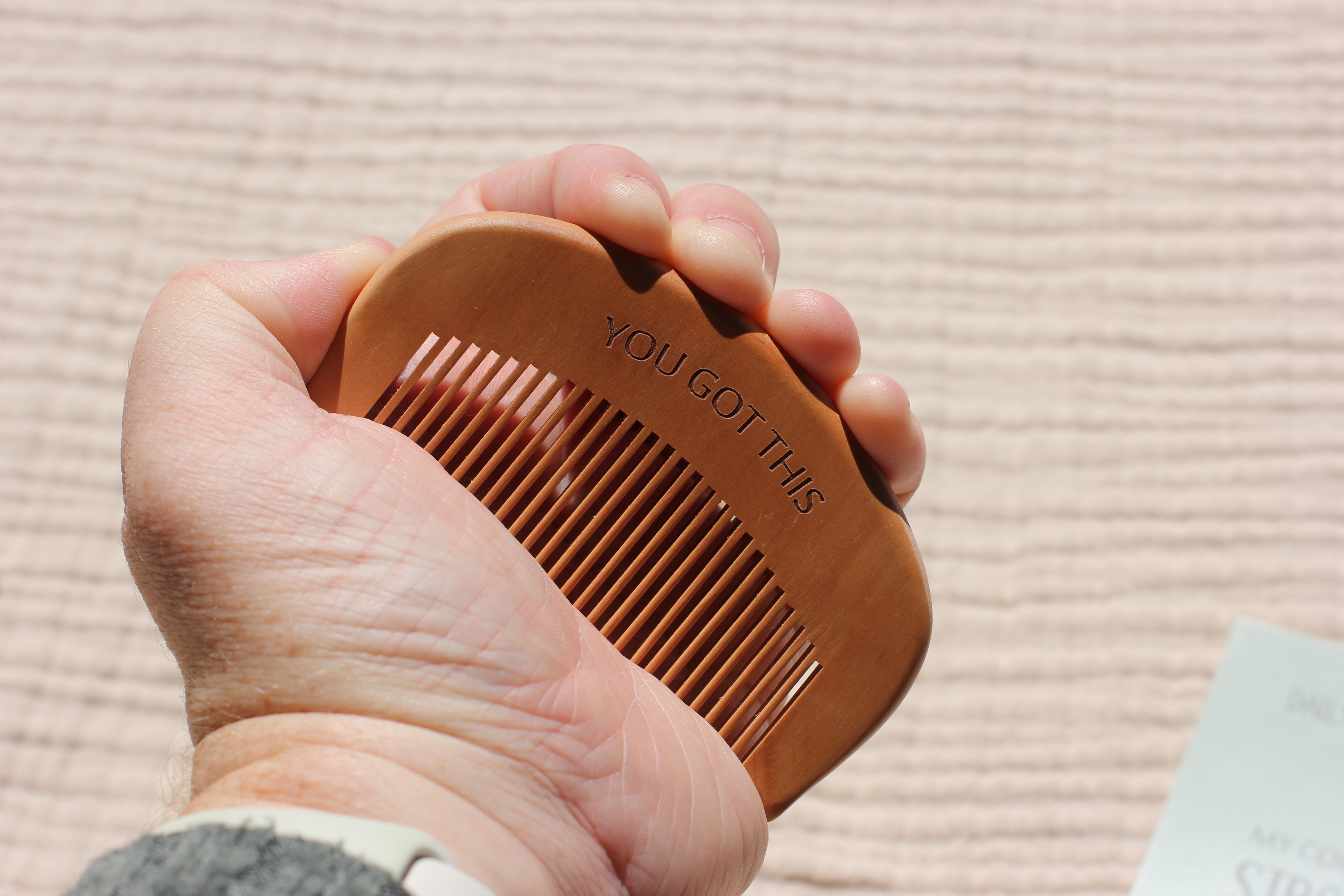 A hand gripping the wooden birth comb engraved with 'You Got This' during a contraction