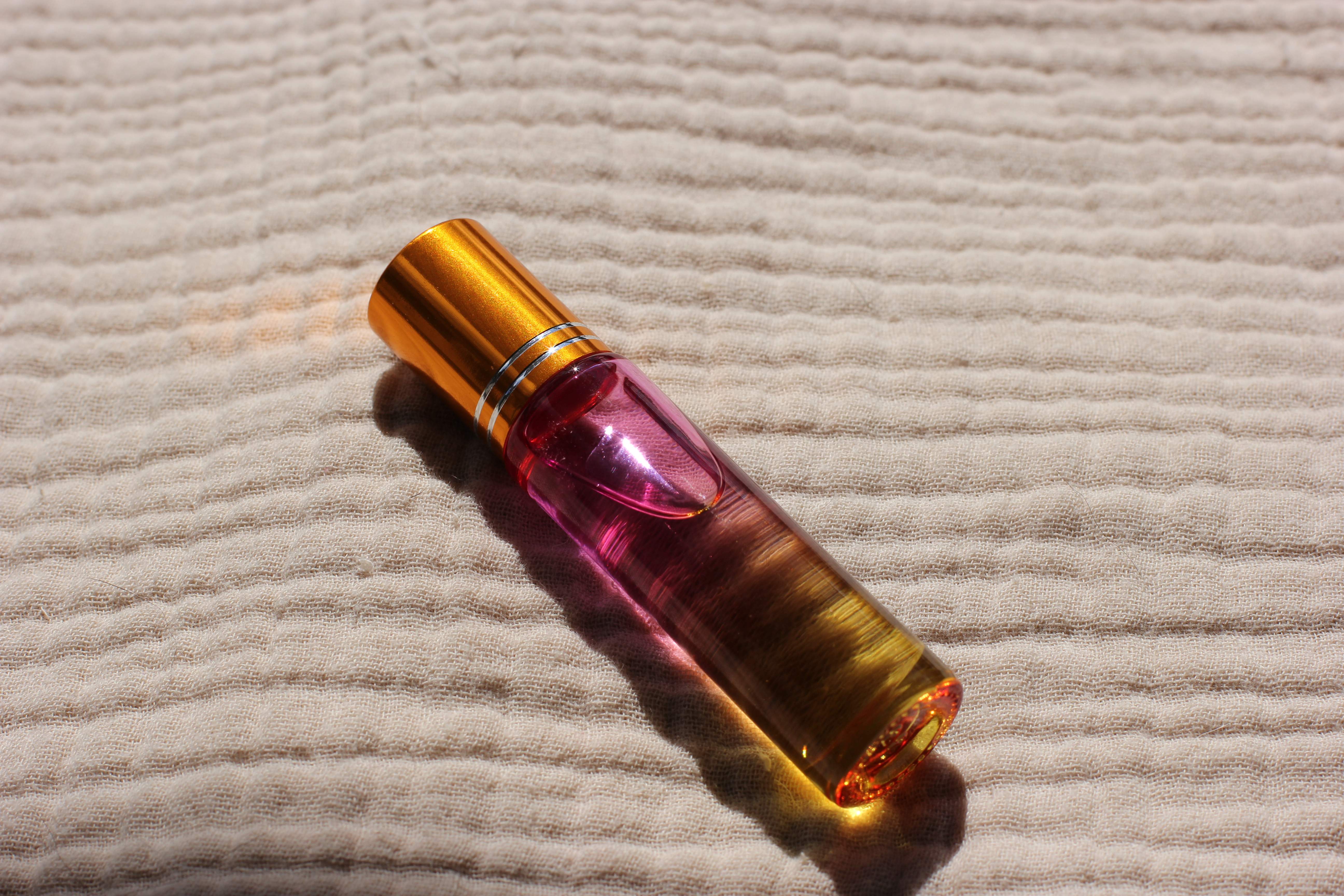 A close-up of the roll-on essential oil labor blend from the Complete Labor Comfort Kit, its amber and pink glass catching the light on a woven blanket