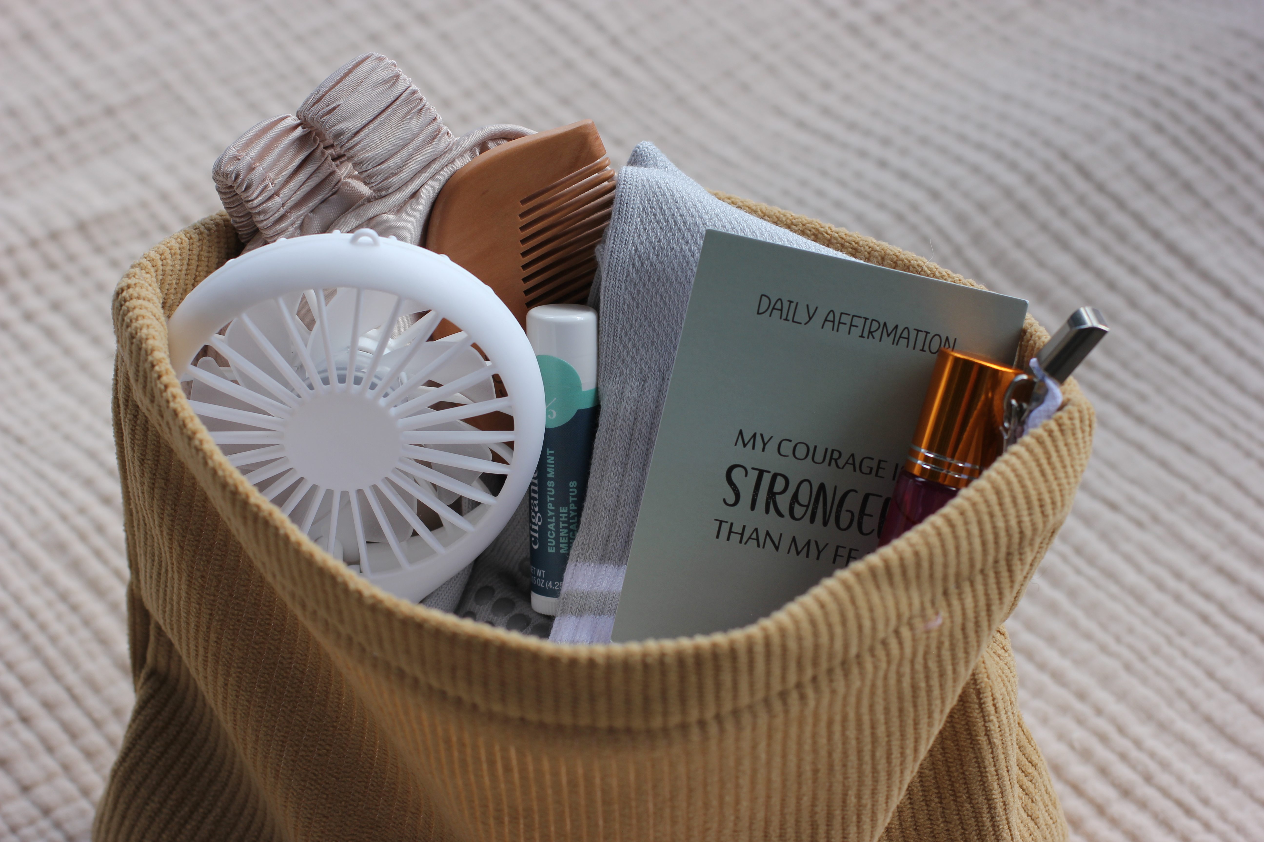 A close-up of the Complete Labor Comfort Kit's contents peeking out of the tan corduroy pouch, including the birth comb, affirmation card, socks, and lip balm