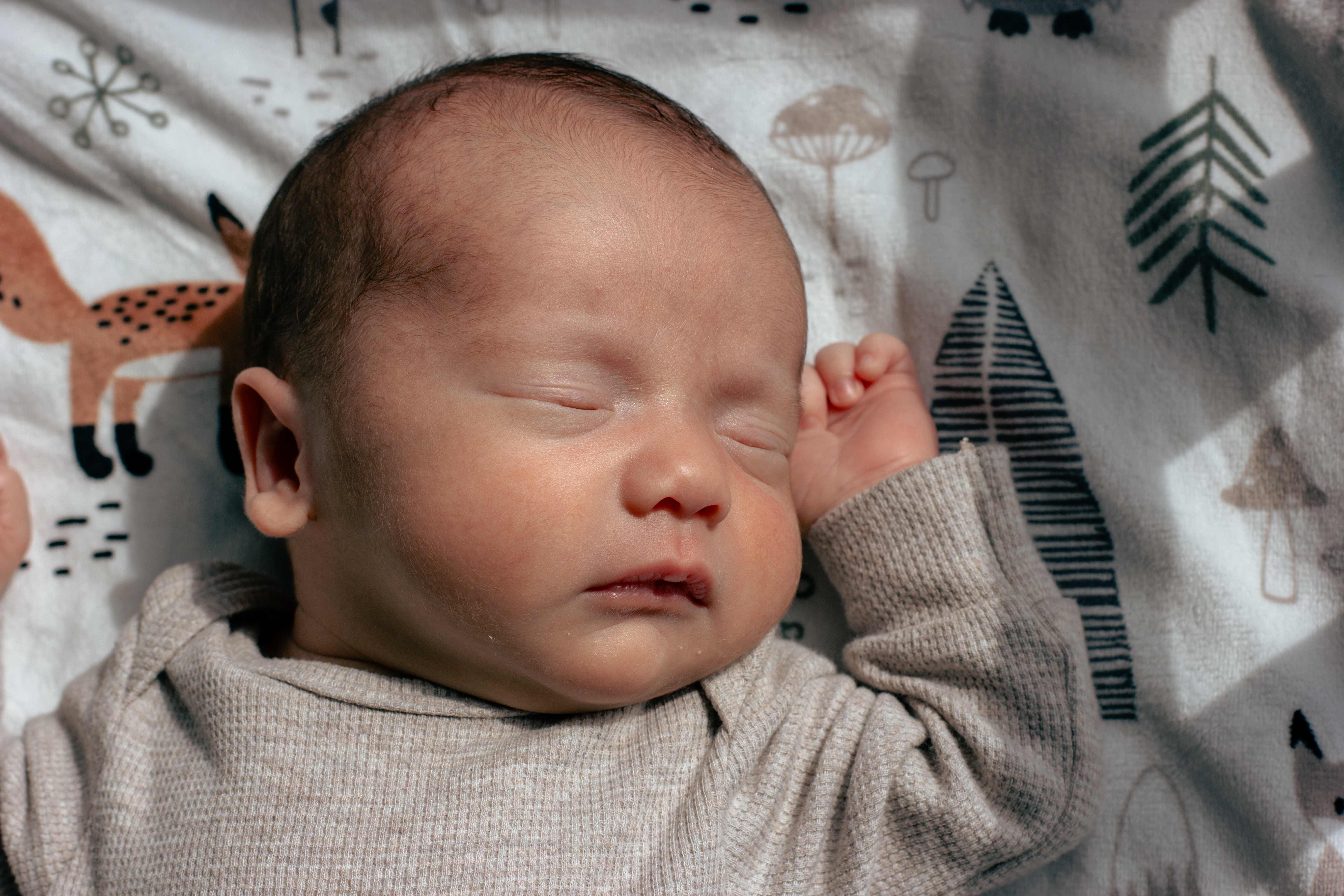 Sleeping newborn in beige outfit on woodland patterned blanket